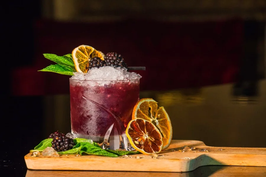 A berry cocktail with crushed ice, mint and dried citrus on a wooden serving board