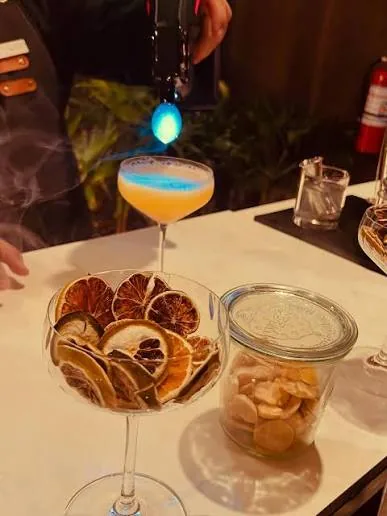 A coupe cocktail being finished beside dried citrus and garnish jars.