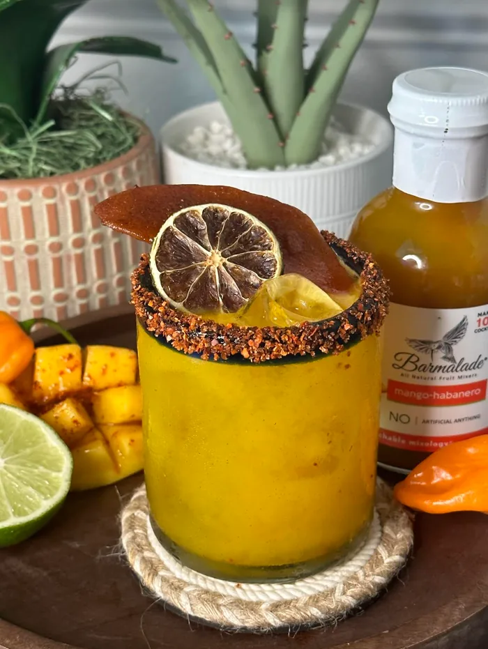 Golden mango cocktail with a chili rim and dried citrus garnish.