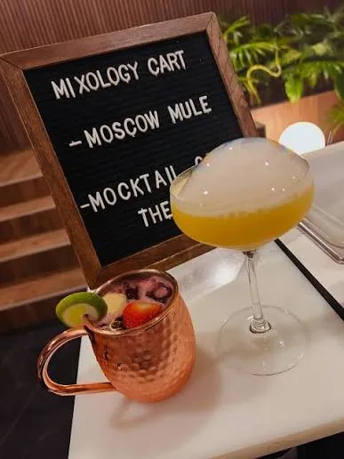 A copper mug and a coupe cocktail beside a mixology cart menu.